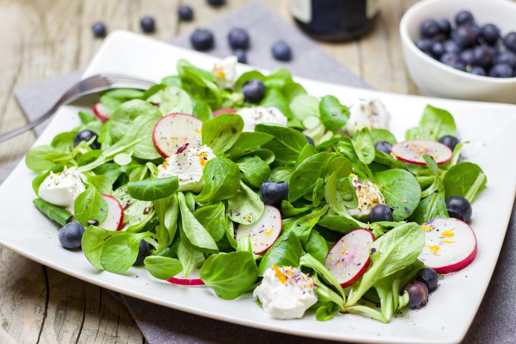 Platte mit grünen Salaten, Blaubeeren und Radieschen - das lässt sich gut vorbereiten und ist auch für Fasten im Job geeignet