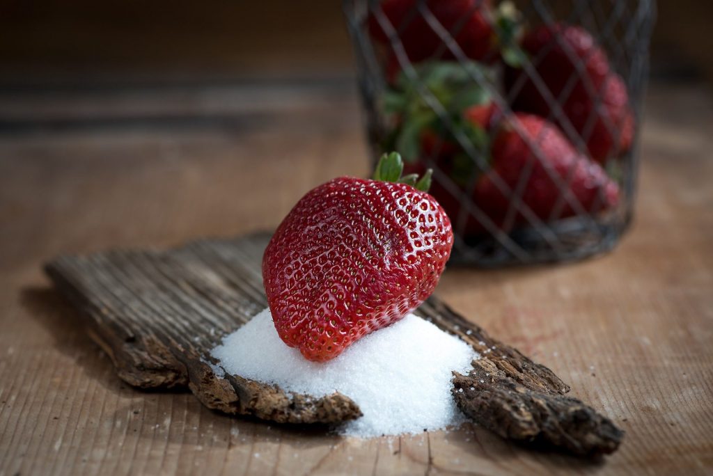 Eine Erdbeere liegt auf einem Häufchen Zucker